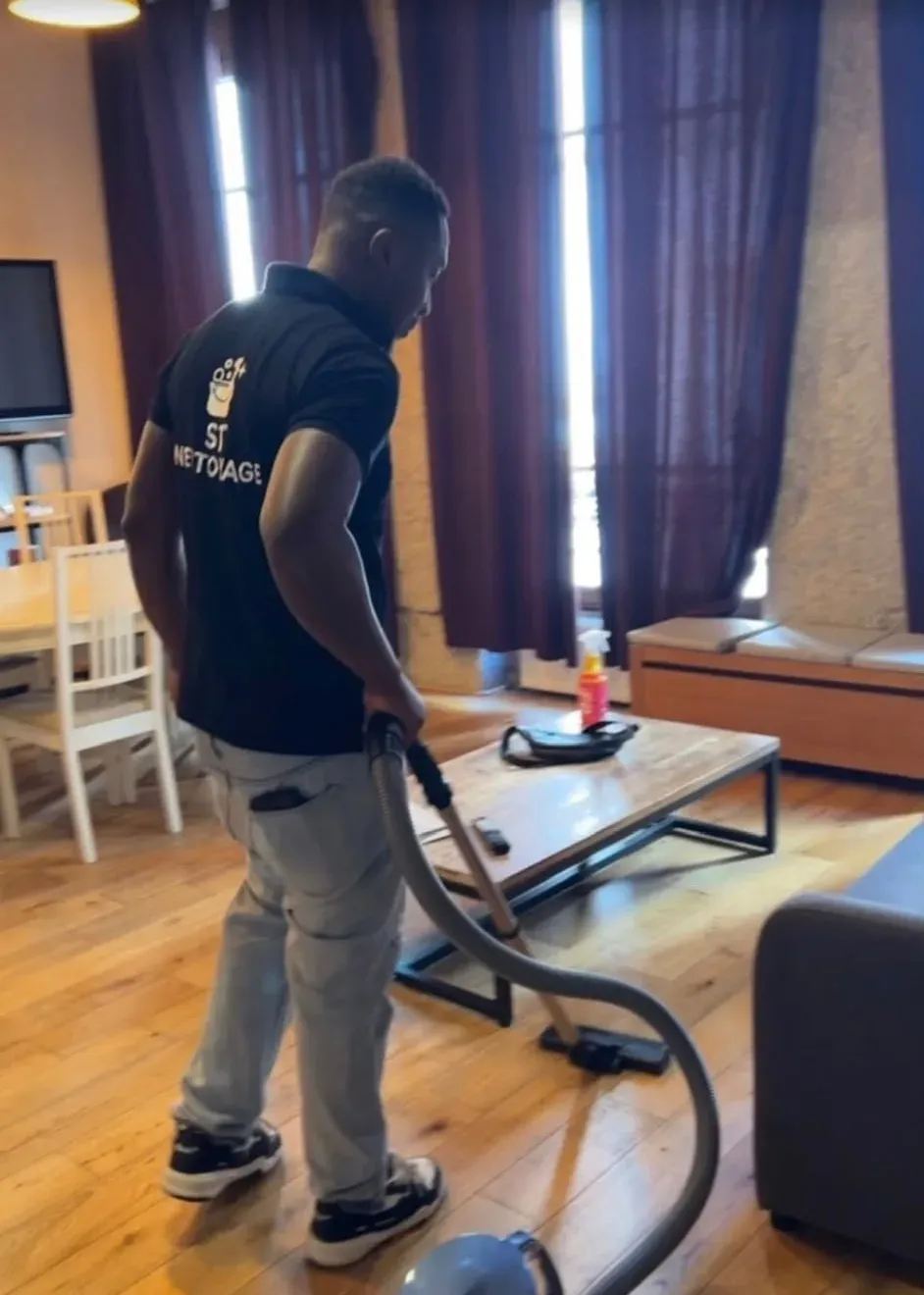Agent ST Nettoyage en polo siglé passant l'aspirateur dans le salon d'un appartement à Lyon